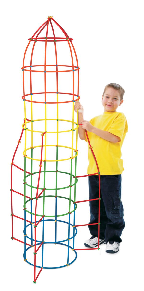 A photo of a Caucasian boy in a yellow shirt, probably seven or eight years old, standing next to a project he completed using the Straws & Connectors 400-Piece Set. He has built a rocket ship shape that is taller than him and has bands of blue, green, yellow, and red straws. The rocket thrusters are made of red straws.