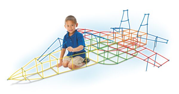 A photo of a Latino boy in a blue shirt, probably five or six years old, kneeling inside a project he completed using the Straws & Connectors 705-Piece Set. He has constructed a jet plane shape that he can fit inside. The jet is made of blue, green, yellow, and red straws.