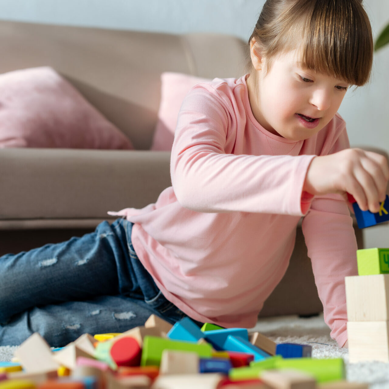 Child with down syndrome playing with toy cubes on floor in cozy room