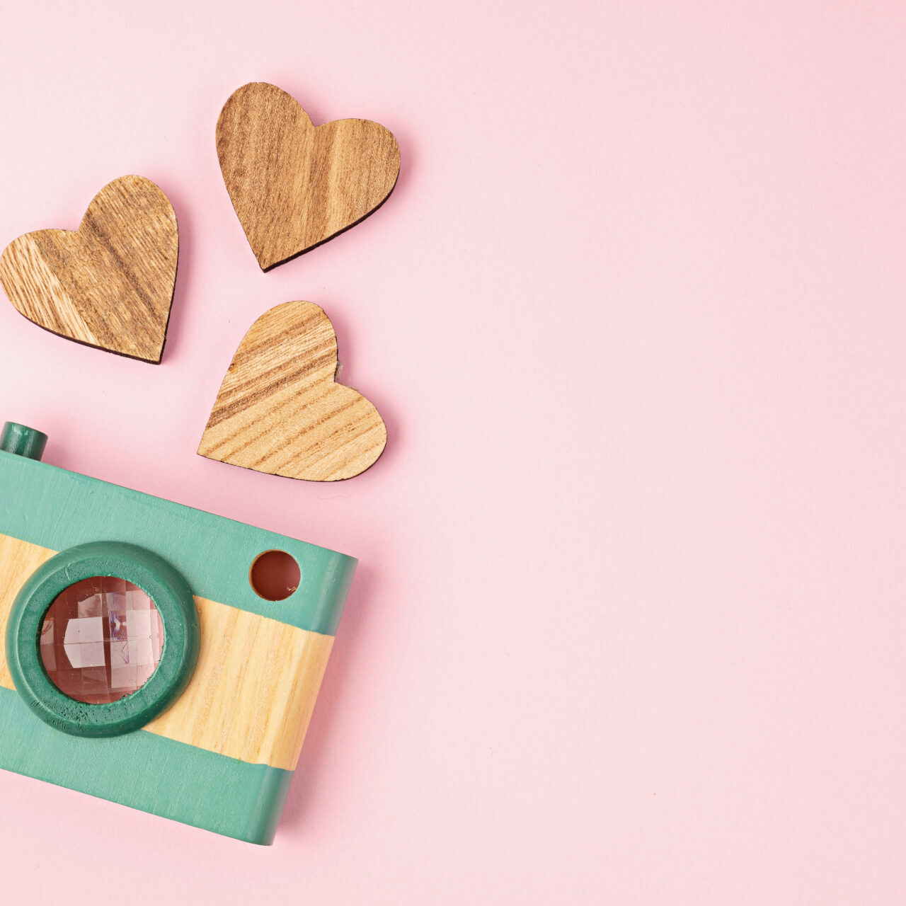 Flat lay with toy wooden camera and hearts over pink background. Social media, posts, likes, followers, online photography classes concept. Top view, copy space.